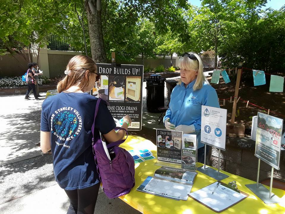 Photo shows one woman talking to another women at a booth on Earth Day at Birmingham Botanical Gardens in Alabama. The topic of the booth is about how oil builds up in drains and clogs them.
