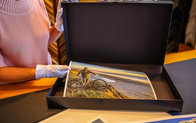 Carla is wearing white cotton gloves to handle a large archival photo while placing it in an acid-free storage container.