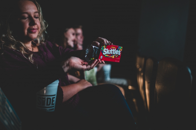 Someone shares Skittles with another person in the theater.