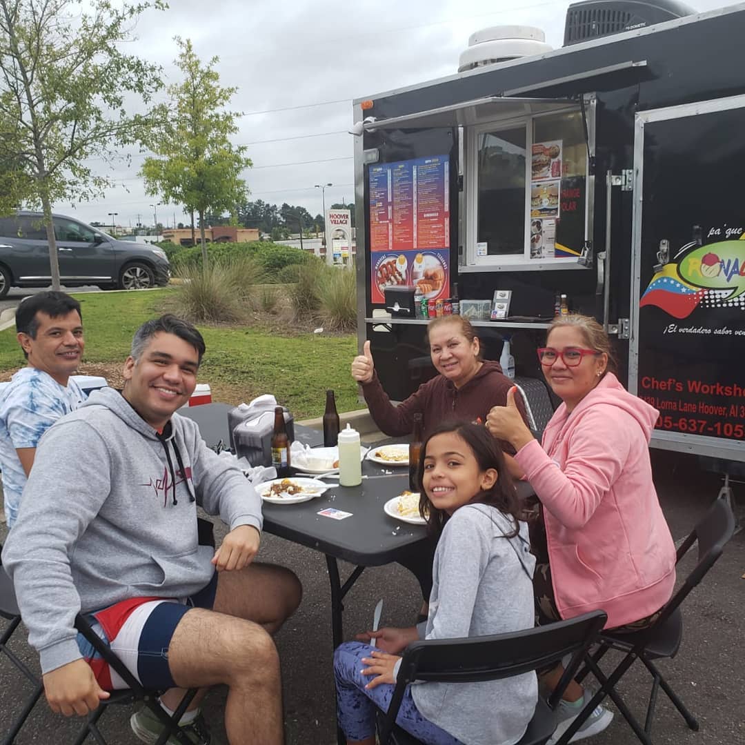 A smiling family sits outside of Pa'Que Ronald food truck