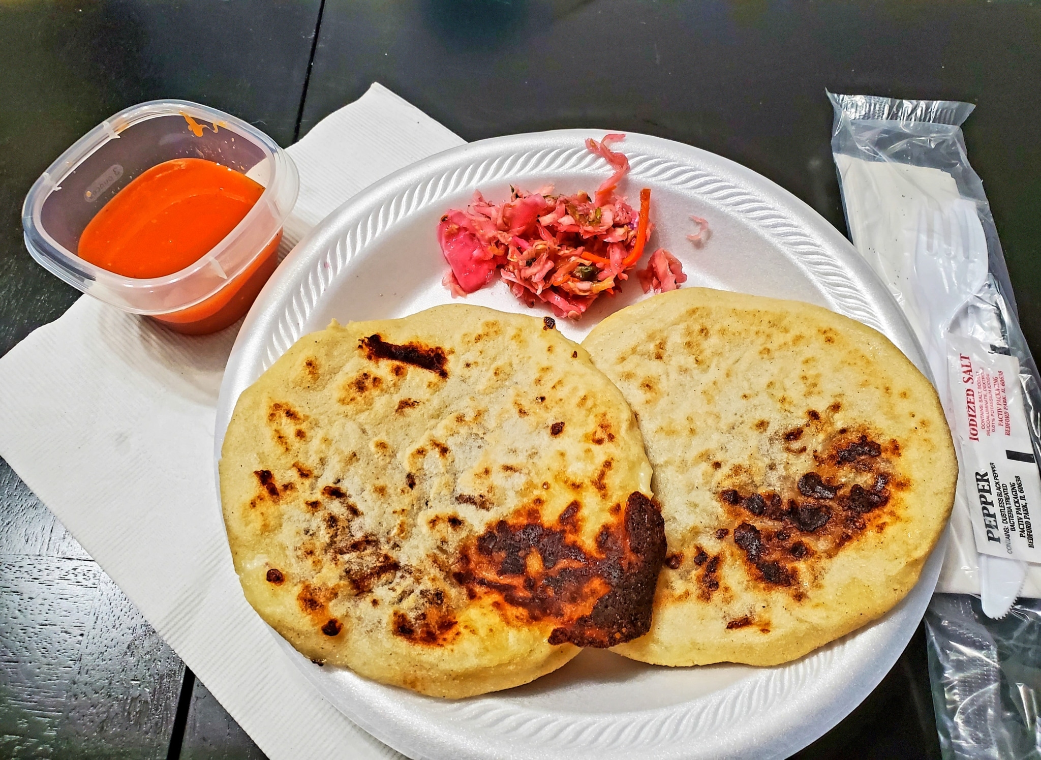 Plate with two pupusas on it and condiments on the side.