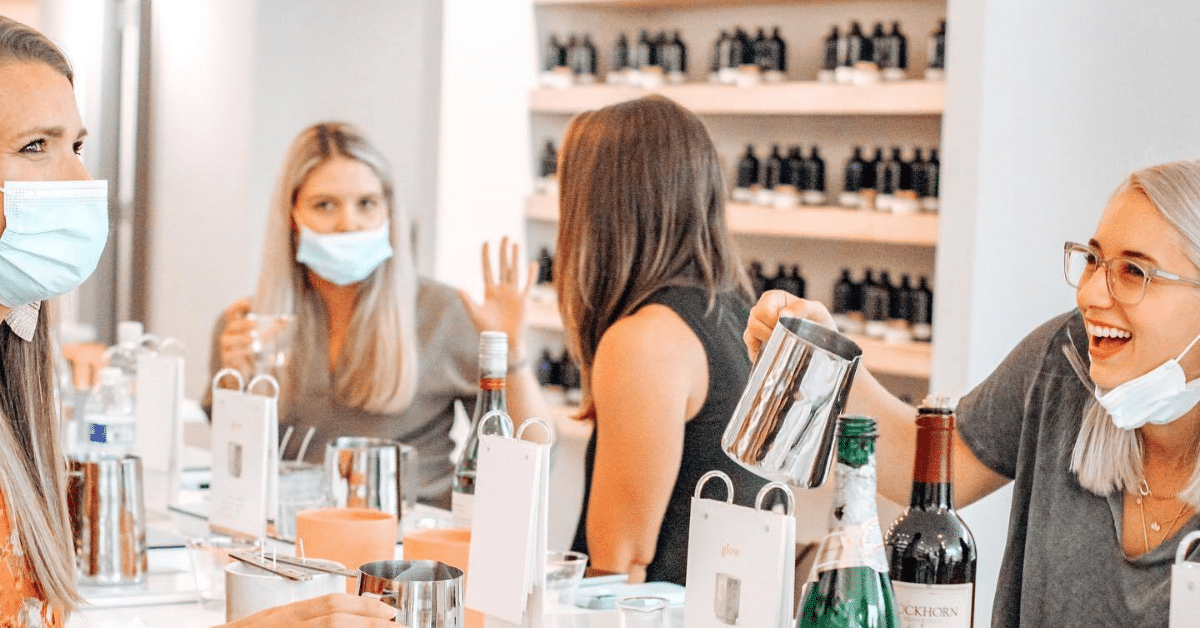 Women laughing and wearing face masks while pouring candles in Paddywax Candle Bar