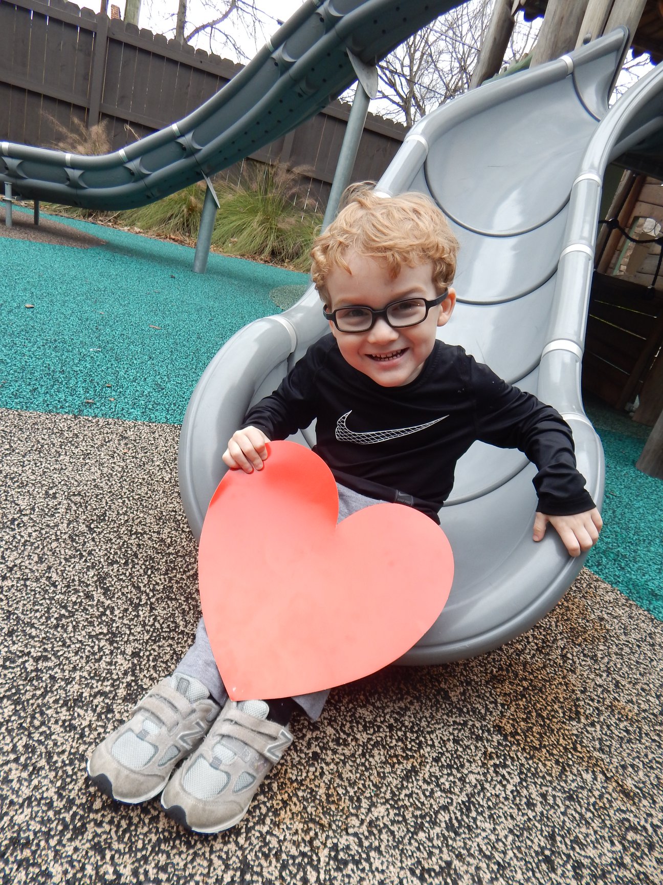 child smiling holding a paper heart, send a valentine to the Ronald McDonald House in Birmingham