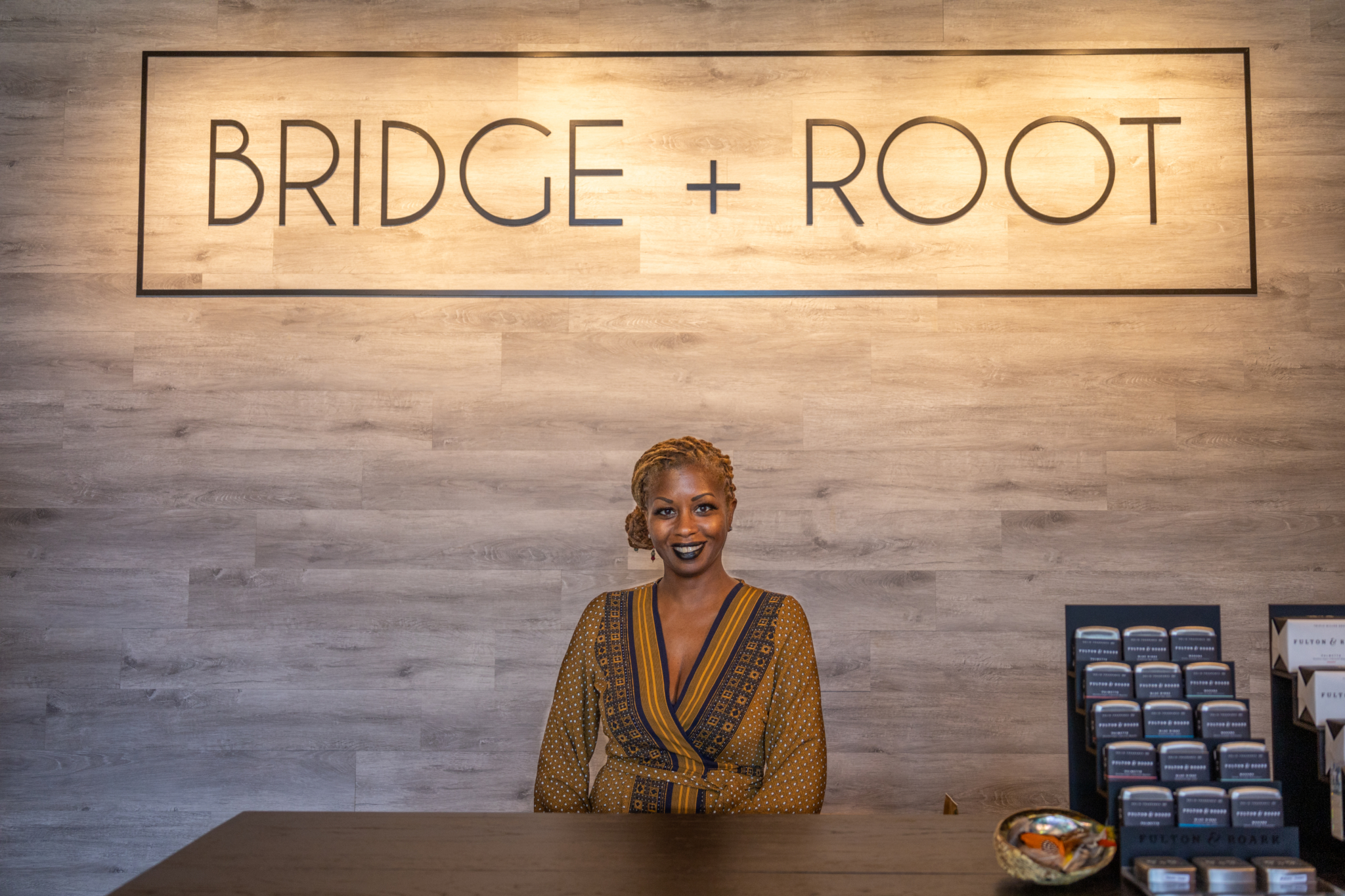 Woman standing behind desk with “Bridge + Root” logo behind her
