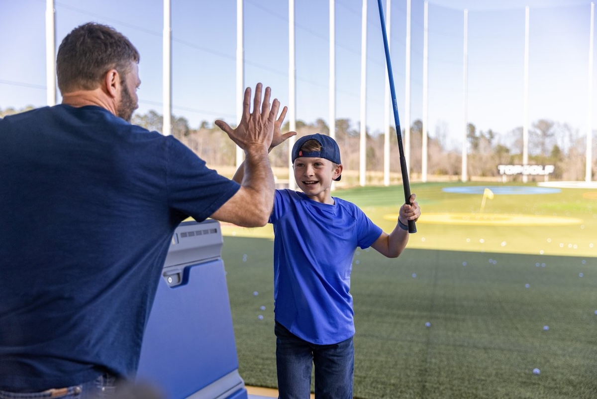 A man gives a young boy a high five after he hit a golf ball at Top Golf in Ridgeland, Mississippi.