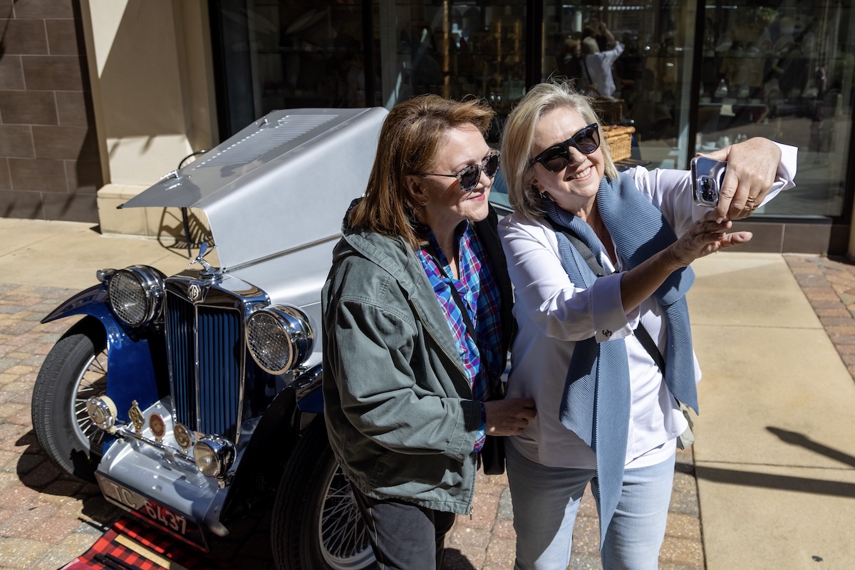Two women take a photo of themselves in front of a classic European car at Euro Fest at Renaissance at Colony Park, a big annual event in Ridgeland, Mississippi, a European getway from Birmingham